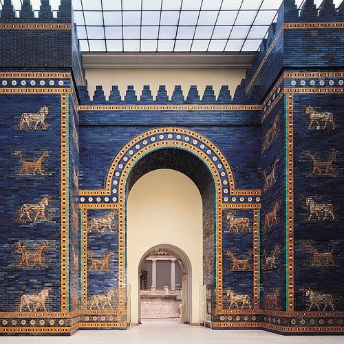 A Porta de Ishtar reconstruída: muralha de tijolos vidrados azuis com touros e dragões em relevo dourado, atravessada por um grande arco.